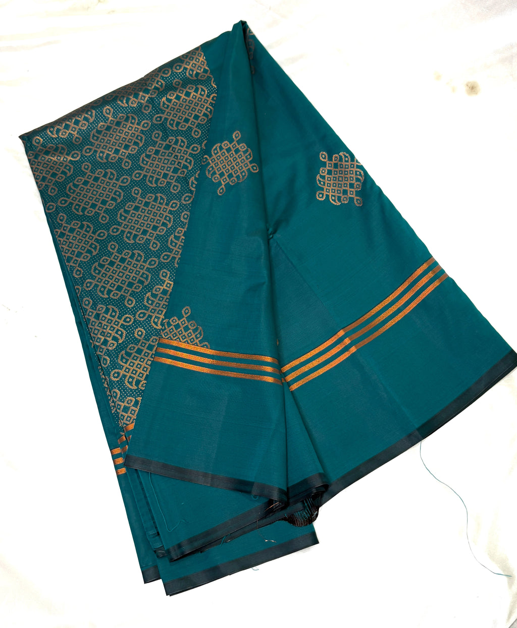 Teal saree with gold kolam patterns on a white background