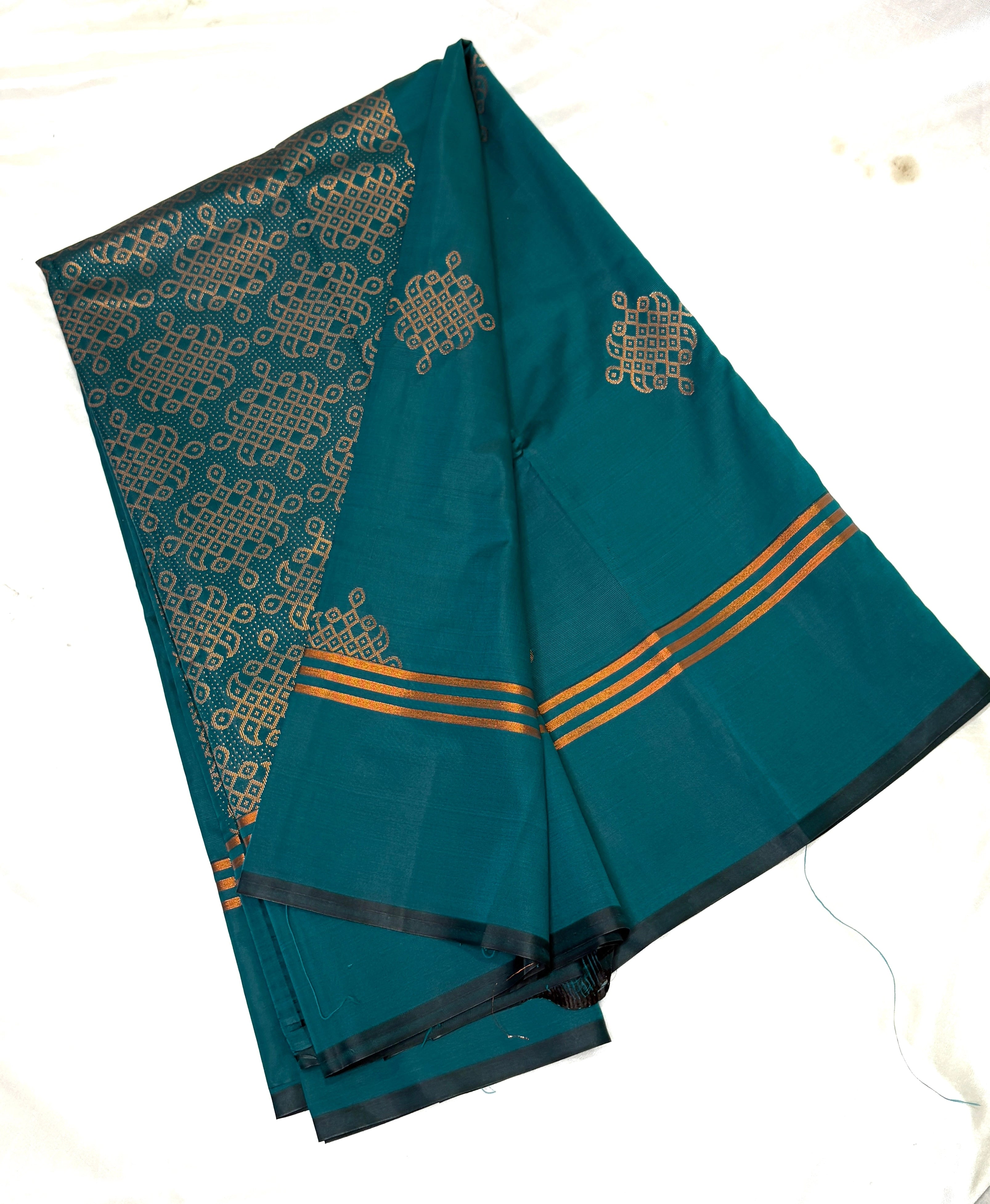Teal saree with gold kolam patterns on a white background